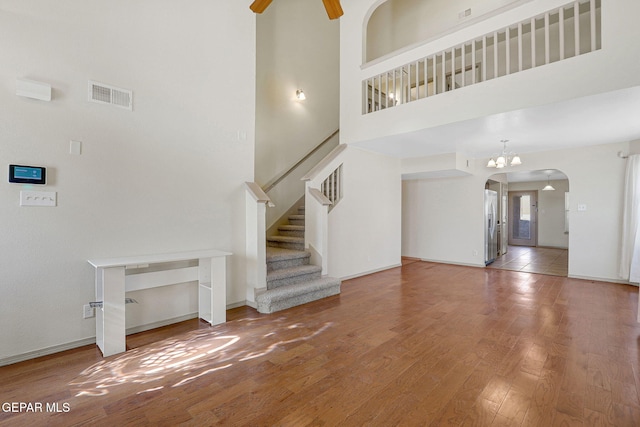 3929 Hueco Valley Dr, El Paso, TX 79938 - unfurnished living room featuring a high ceiling, arched walkways, stairs, wood finished floors, and visible vents