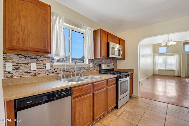 3929 Hueco Valley Dr, El Paso, TX 79938 - kitchen featuring brown cabinetry, decorative backsplash, a sink, a notable chandelier, and stainless steel appliances