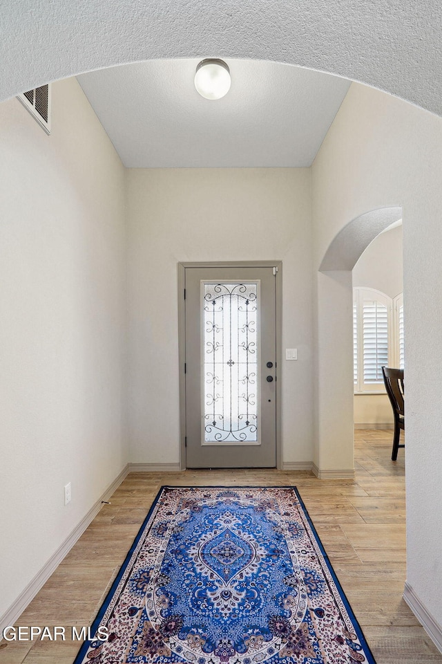 foyer with arched walkways, baseboards, and wood finished floors