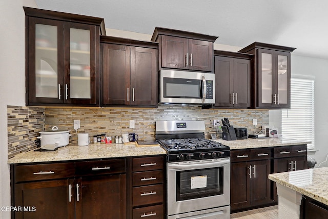 kitchen featuring light stone countertops, backsplash, dark brown cabinets, and stainless steel appliances