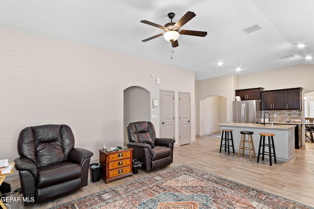 living room featuring arched walkways, a ceiling fan, visible vents, and light wood-type flooring