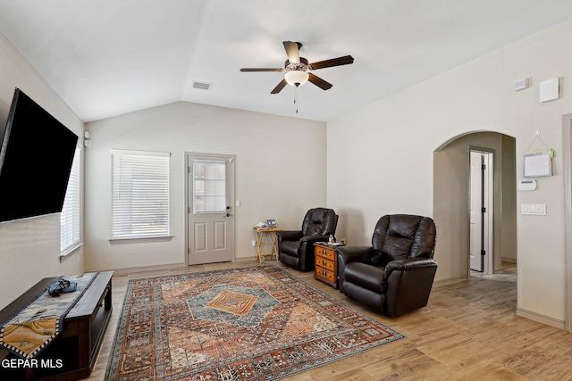 living area with arched walkways, light wood-style flooring, a ceiling fan, vaulted ceiling, and visible vents
