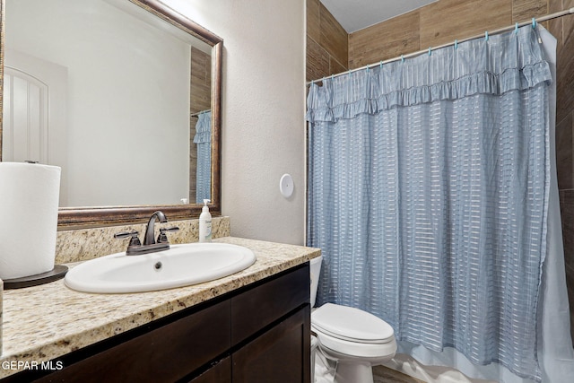 full bath with vanity, a textured wall, and toilet