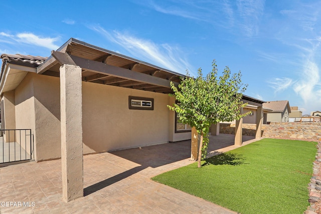 rear view of property featuring a lawn, stucco siding, and a patio area