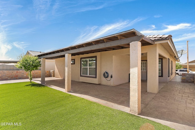 rear view of house featuring fence, stucco siding, a yard, and a patio area
