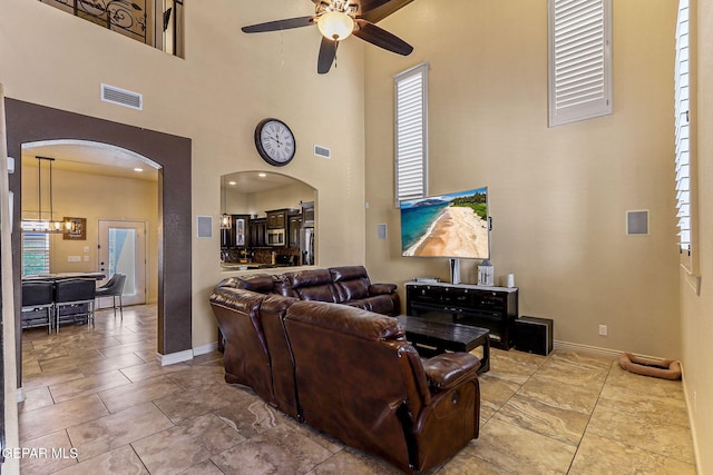 living area with visible vents, arched walkways, a ceiling fan, a high ceiling, and baseboards