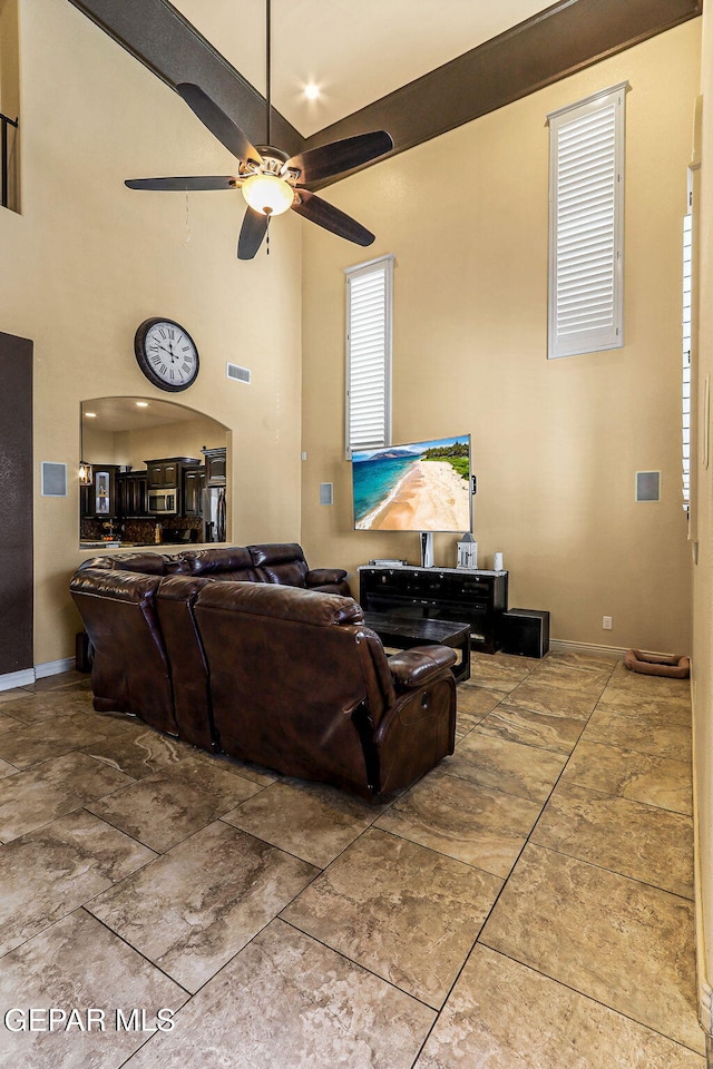 living room with a ceiling fan, baseboards, visible vents, and a high ceiling
