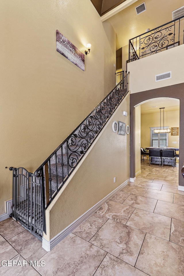 staircase with visible vents, baseboards, a towering ceiling, and arched walkways