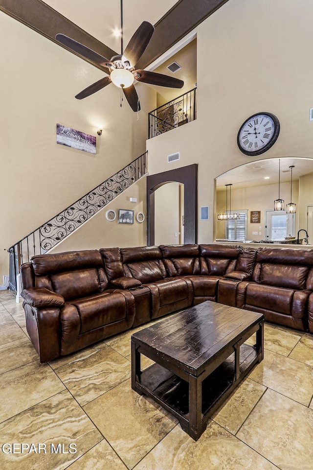 living area featuring arched walkways, visible vents, a ceiling fan, and a towering ceiling