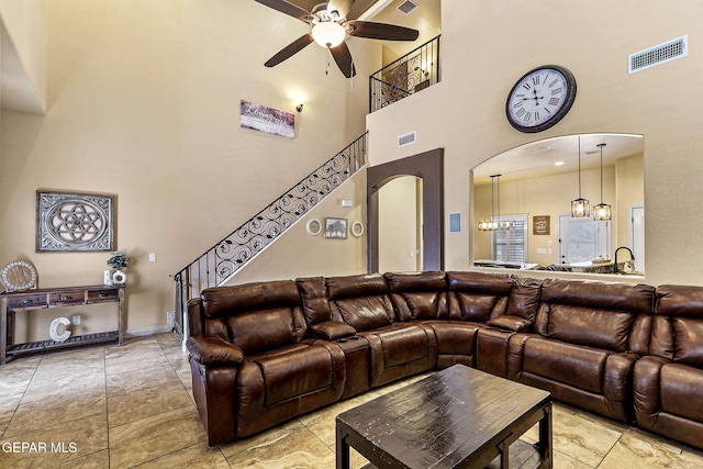 living room featuring a ceiling fan, a high ceiling, visible vents, arched walkways, and stairs