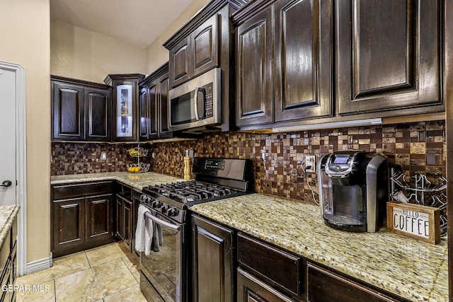 kitchen featuring tasteful backsplash, dark brown cabinetry, glass insert cabinets, light stone countertops, and appliances with stainless steel finishes