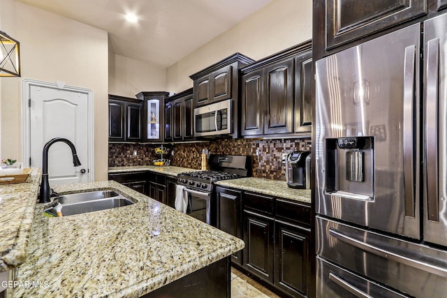 kitchen with a sink, light stone counters, decorative backsplash, glass insert cabinets, and appliances with stainless steel finishes
