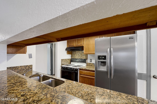 kitchen with stainless steel fridge, gas range oven, under cabinet range hood, a sink, and backsplash
