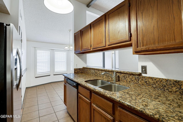 kitchen with brown cabinetry, a textured ceiling, a sink, light tile patterned floors, and stainless steel appliances