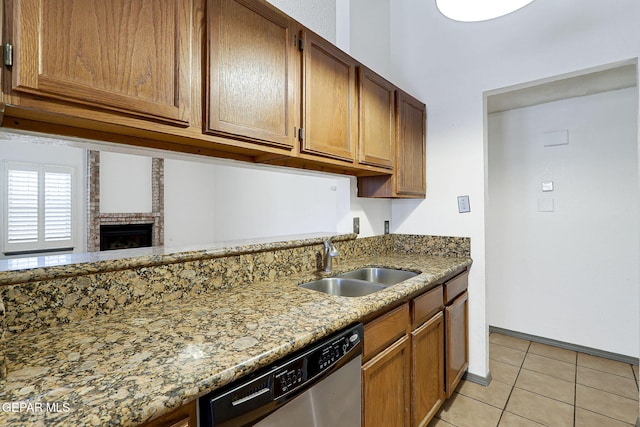 kitchen with stainless steel dishwasher, light tile patterned flooring, light stone counters, and a sink
