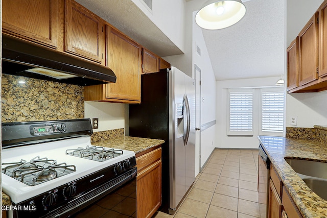 kitchen with light tile patterned flooring, under cabinet range hood, brown cabinets, appliances with stainless steel finishes, and vaulted ceiling