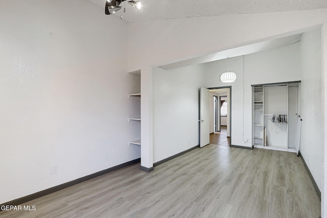 unfurnished bedroom with a closet, a high ceiling, baseboards, and light wood-type flooring