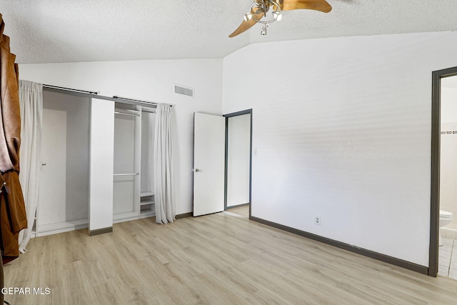 unfurnished bedroom with a textured ceiling, vaulted ceiling, visible vents, and light wood-type flooring