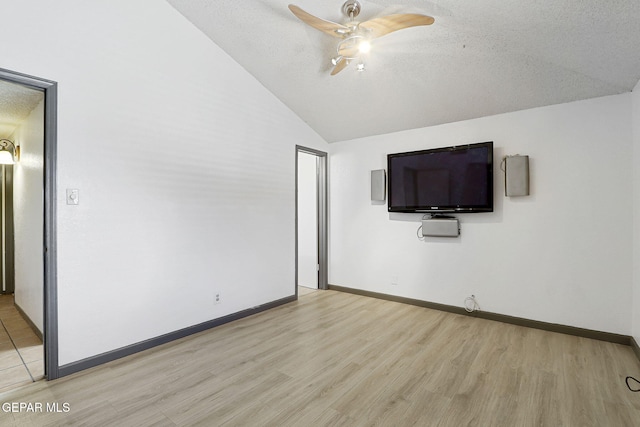 unfurnished bedroom with ceiling fan, a textured ceiling, light wood-style flooring, baseboards, and lofted ceiling