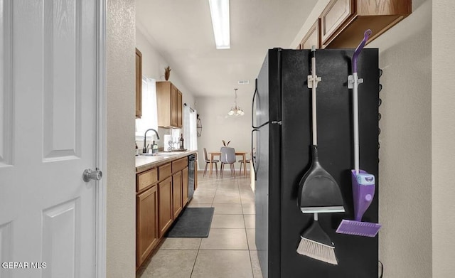 kitchen featuring brown cabinets, a sink, light countertops, freestanding refrigerator, and light tile patterned flooring