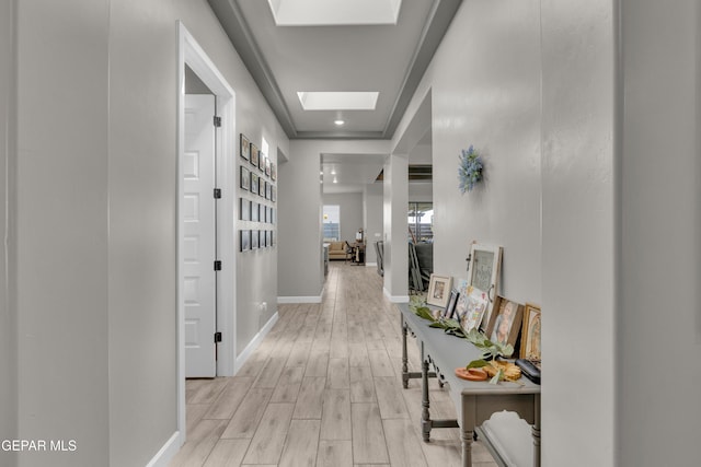 corridor featuring baseboards, light wood-style flooring, and a skylight