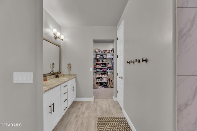 full bathroom featuring double vanity, wood finished floors, baseboards, a spacious closet, and a sink