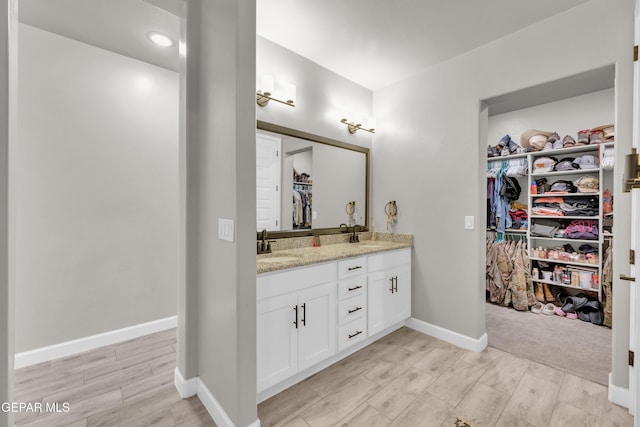 bathroom featuring double vanity, a walk in closet, wood finished floors, a sink, and baseboards