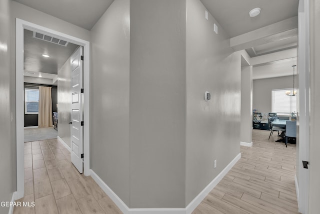 corridor with an inviting chandelier, baseboards, wood tiled floor, and visible vents