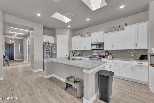 kitchen featuring decorative backsplash, light wood-style floors, a sink, appliances with stainless steel finishes, and a skylight