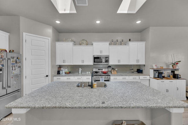 kitchen with appliances with stainless steel finishes, a sink, decorative backsplash, a skylight, and visible vents