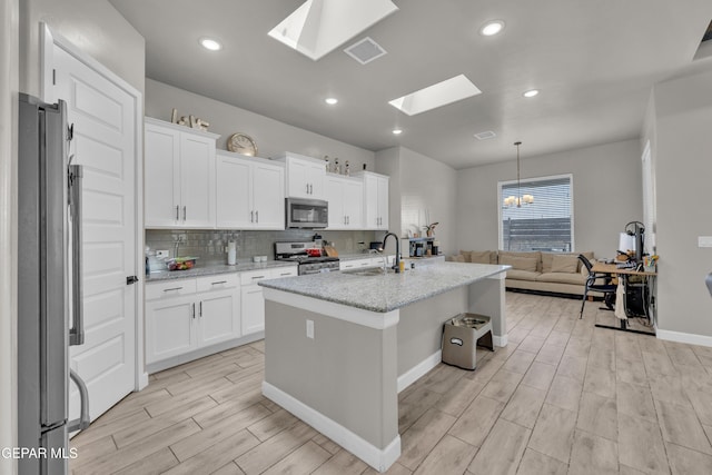 kitchen featuring light stone counters, a sink, light wood-style floors, stainless steel appliances, and a skylight