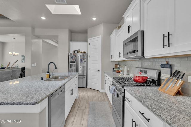kitchen featuring appliances with stainless steel finishes, light stone countertops, a center island with sink, a sink, and white cabinets