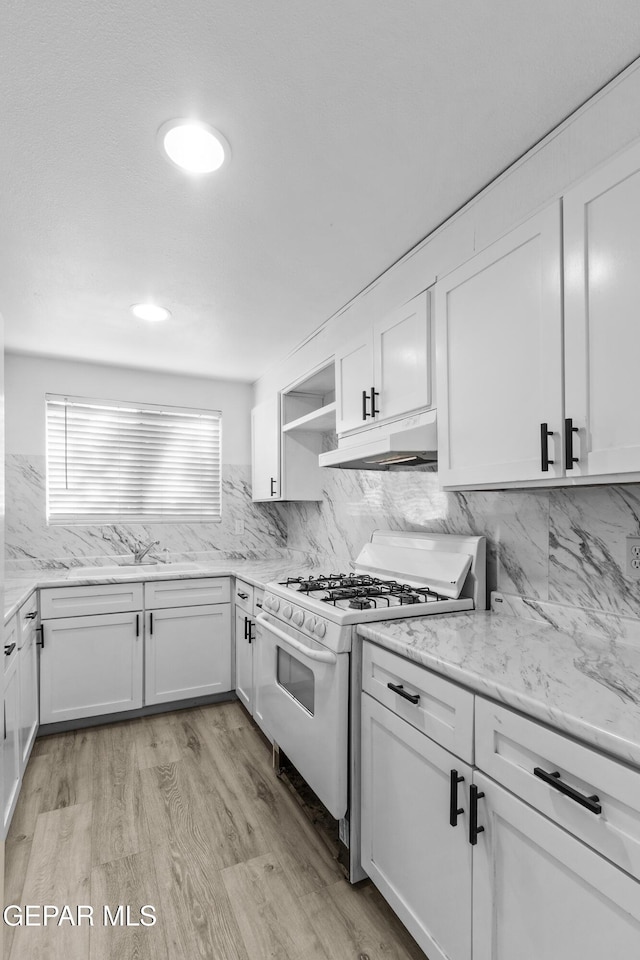 kitchen with white gas range oven, under cabinet range hood, white cabinets, and tasteful backsplash