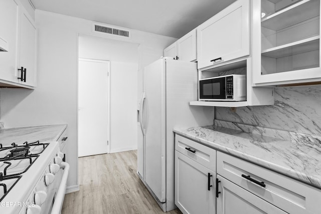 kitchen with visible vents, light stone countertops, white appliances, light wood-style floors, and white cabinetry