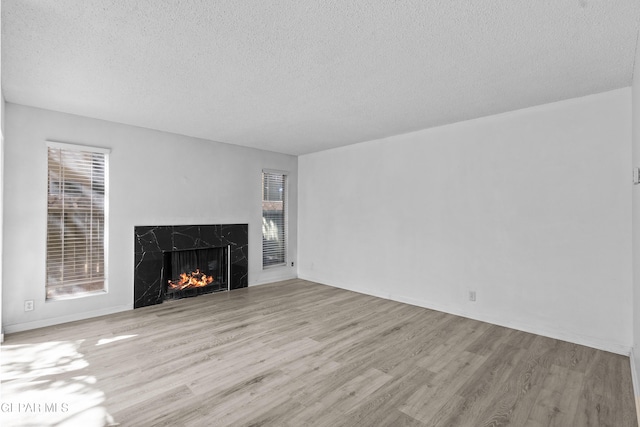 unfurnished living room featuring baseboards, a high end fireplace, a textured ceiling, and wood finished floors