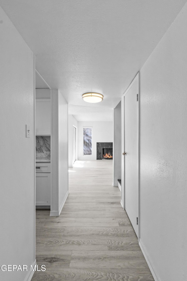 corridor featuring light wood-style floors, baseboards, and a textured ceiling
