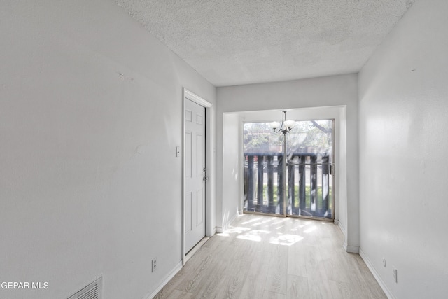 hall featuring an inviting chandelier, a textured ceiling, and light wood-style flooring