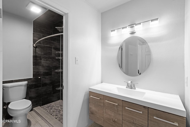 bathroom with toilet, tiled shower, and vanity