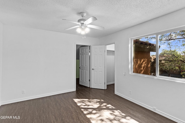 unfurnished bedroom featuring baseboards, a textured ceiling, dark wood finished floors, and a spacious closet
