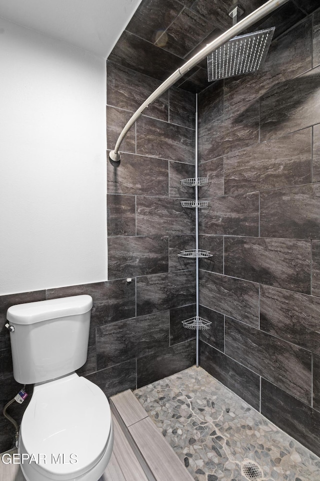 full bathroom featuring toilet, tile walls, wainscoting, and tiled shower