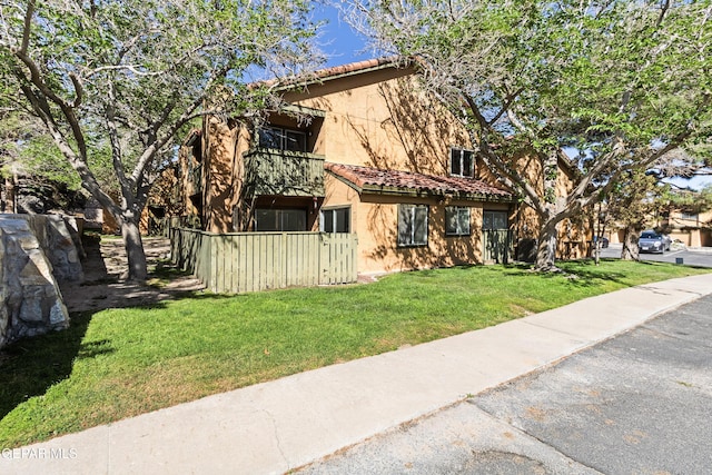 view of front of home with a front lawn, fence, a balcony, stucco siding, and a tiled roof