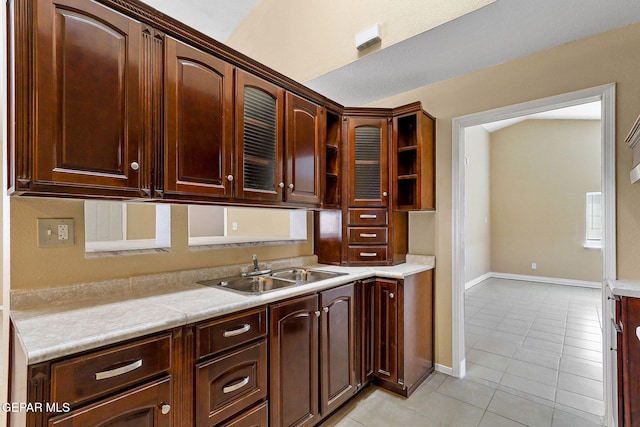 kitchen with a sink, light tile patterned floors, baseboards, light countertops, and glass insert cabinets