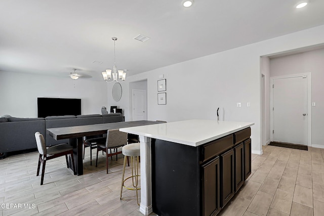kitchen with a center island, light wood-type flooring, light countertops, ceiling fan with notable chandelier, and open floor plan