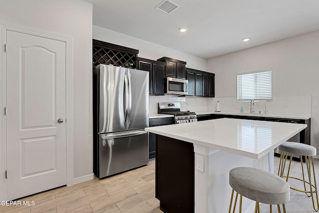 kitchen with a breakfast bar, dark cabinets, stainless steel appliances, decorative backsplash, and a kitchen island