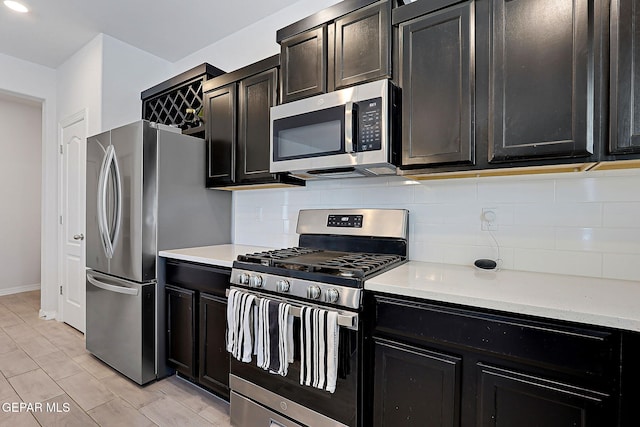 kitchen featuring appliances with stainless steel finishes, baseboards, backsplash, and dark cabinetry