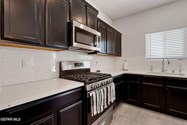 kitchen with dark brown cabinetry, tasteful backsplash, a sink, light stone counters, and stainless steel appliances