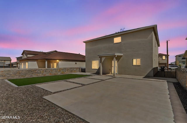 back of house at dusk featuring a fenced backyard, a patio, and stucco siding