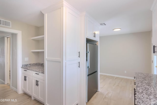1721 Villa Santos Cir, El Paso, TX 79935 - kitchen with open shelves, light stone countertops, light wood-style floors, stainless steel fridge, and white cabinets