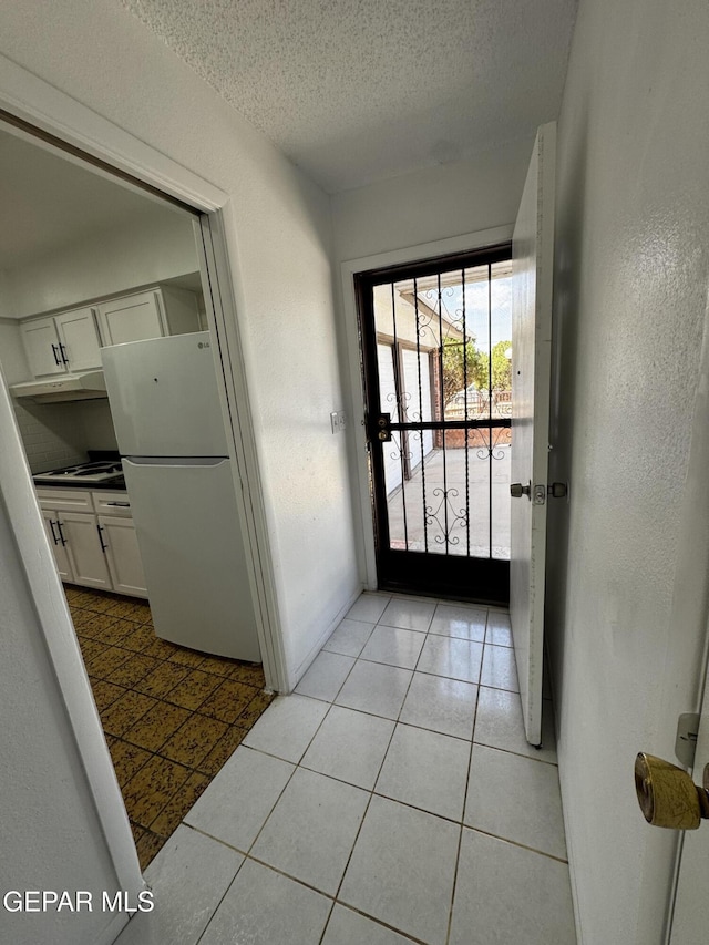 doorway to outside featuring a textured ceiling, light tile patterned flooring, and baseboards