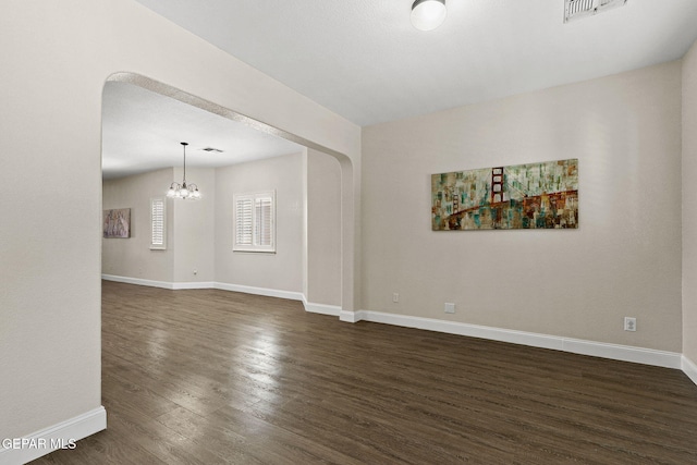 empty room featuring visible vents, dark wood finished floors, baseboards, and a notable chandelier